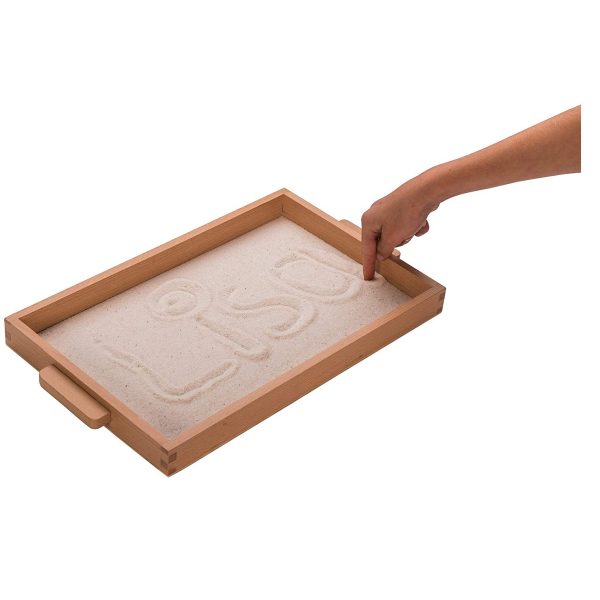 Tablett aus Holz mit Sand befüllt. Eine Hand zieht Spuren im Sand.