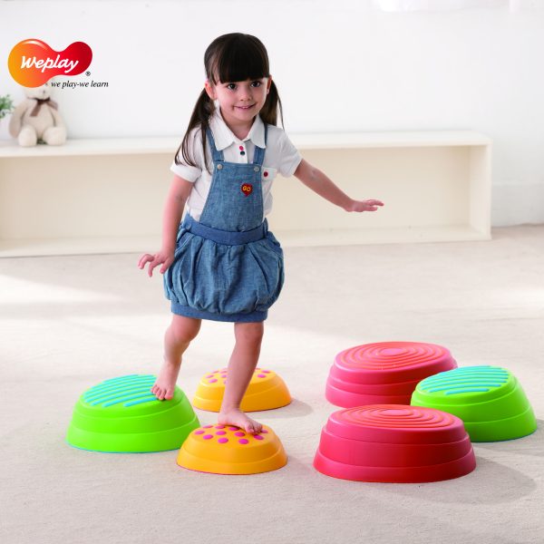 Kind überquert Kunststoffsteine die in einem Kreis gelegt sind.